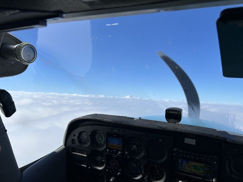 Cockpit view above the clouds showing a Garmin G5 electronic flight instrument, traditional round gauges and a GPS moving map on the instrument panel
